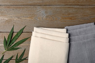 Hemp cloths and green leaves on wooden table, flat lay. Space for text