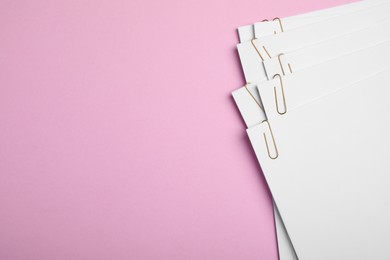Sheets of paper with clips on pink background, top view. Space for text