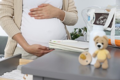 Pregnant woman near chest of drawers with packed bag for maternity hospital indoors, closeup