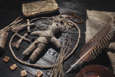 Female voodoo doll with pins surrounded by ceremonial items on black wooden background