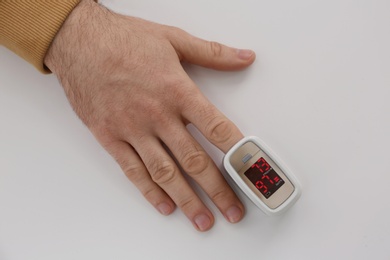 Photo of Man measuring oxygen level with modern fingertip pulse oximeter at white table, top view