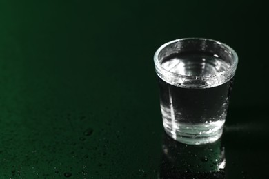 Glass of vodka on dark wet table, space for text