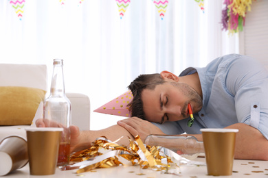 Young man with festive cap sleeping at table after party