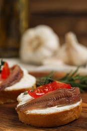 Photo of Delicious sandwiches with cream cheese, anchovies and tomatoes on wooden board, closeup. Space for text