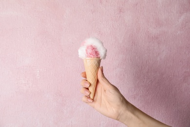 Woman holding ice cream cone with fluffy cotton candy on color background, closeup