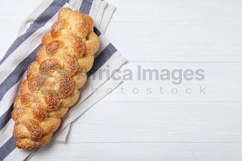 Homemade braided bread with sesame seeds on white wooden table, top view and space for text. Traditional challah