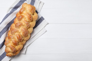 Homemade braided bread with sesame seeds on white wooden table, top view and space for text. Traditional challah