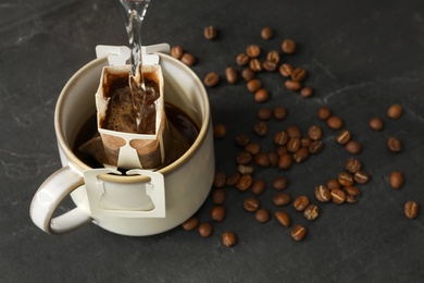 Pouring hot water into cup with drip coffee bag on black table, closeup