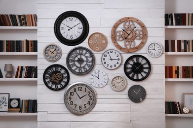 Collection of different clocks between bookshelves in room. Interior design