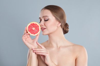 Photo of Young woman with cut grapefruit on grey background. Vitamin rich food