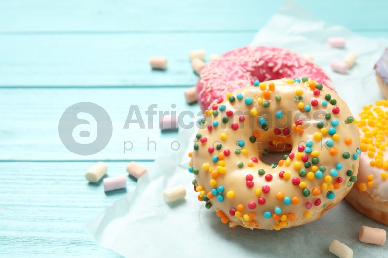 Photo of Delicious glazed donuts on blue wooden table, closeup. Space for text