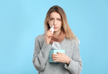 Sick young woman using nasal spray on light blue background