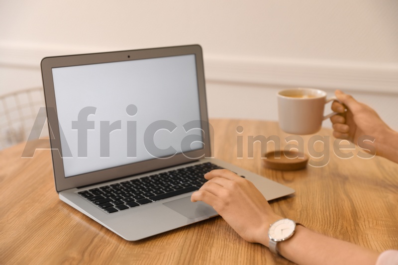 Young blogger with cup of coffee working at table in cafe, closeup