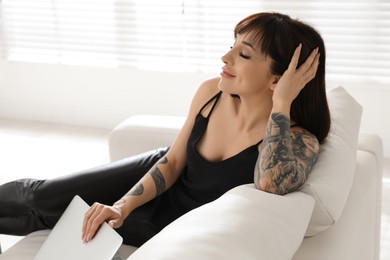 Photo of Beautiful woman with tattoos on arms resting in living room