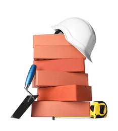 Photo of Many red bricks, trowel, hard hat and tape measure on white background