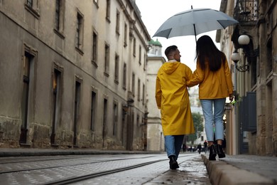 Photo of Lovely young couple with umbrella walking under rain on city street, back view