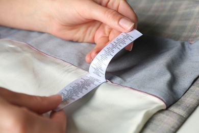 Woman reading clothing label with content information on light garment, closeup