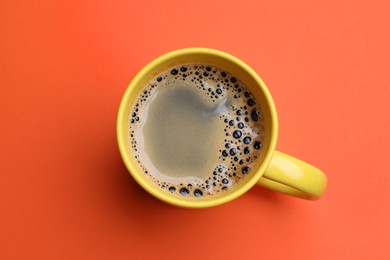 Photo of Yellow mug of freshly brewed hot coffee on orange background, top view