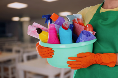 Woman holding basin with cleaning supplies at school canteen, closeup