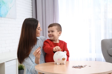 Happy mother and son with piggy bank and money at home