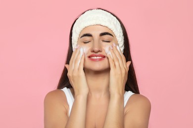 Beautiful woman applying cleansing foam onto face on pink background