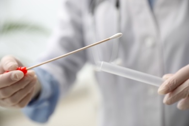 Doctor holding buccal cotton swab and tube for DNA test in clinic, closeup