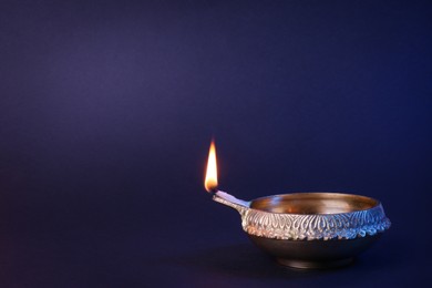 Photo of Lit diya lamp on purple background, space for text. Diwali celebration