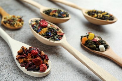 Different kinds of dry herbal tea in wooden spoons on light grey table, closeup