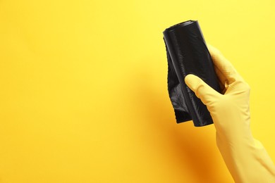 Janitor in rubber glove holding roll of black garbage bags over yellow background, top view. Space for text
