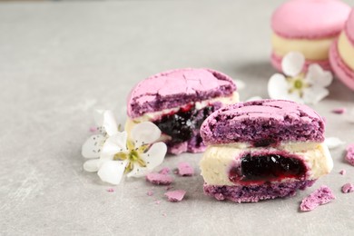 Photo of Halves of delicious violet macaron and flowers on light grey table, closeup. Space for text