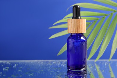 Bottle of face serum on wet surface against blue background, closeup. Space for text