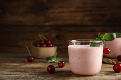 Tasty fresh milk shake with cherries on wooden table. Space for text