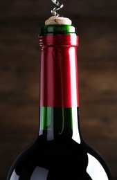 Opening wine bottle with corkscrew on dark brown background, closeup