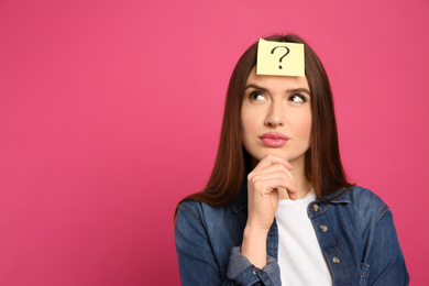 Pensive woman with question mark sticker on forehead against pink background. Space for text