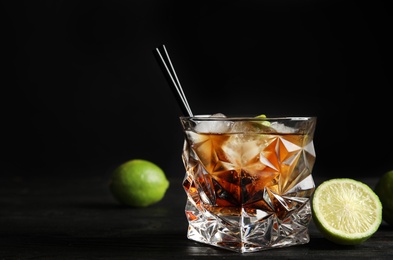 Glass of cocktail with cola, ice and cut lime on table against black background. Space for text