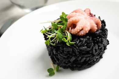 Delicious black risotto with baby octopus in plate, closeup