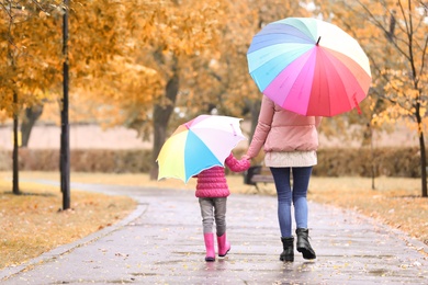 Mother and daughter with umbrellas taking walk in autumn park on rainy day