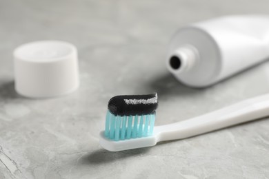 Brush with charcoal toothpaste on light grey table, closeup