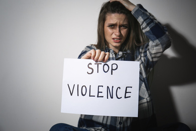 Crying young woman with sign STOP VIOLENCE near white wall