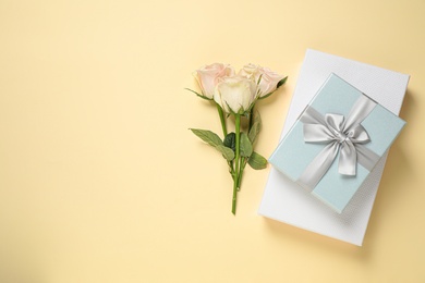 Elegant gift boxes and beautiful flowers on beige background, flat lay. Space for text