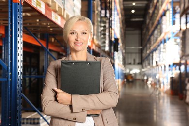 Happy manager holding clipboard in warehouse with lots of products. Space for text