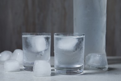 Shot glasses and bottle of vodka with ice cubes on light grey table