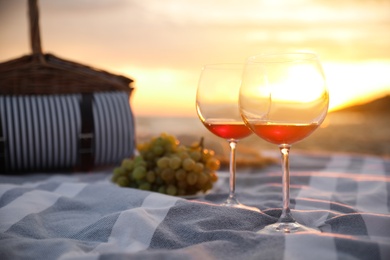Blanket with glasses of wine and food on beach at sunset. Romantic picnic for couple