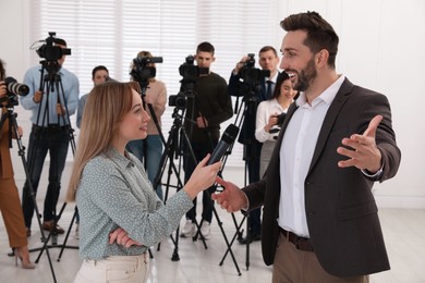 Photo of Professional young journalist interviewing businessman and group of video camera operators on background