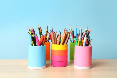 Holders with different school stationery on wooden table against light blue background. Back to school