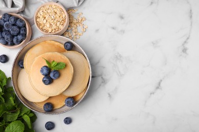 Tasty oatmeal pancakes with blueberries on white marble table, flat lay. Space for text