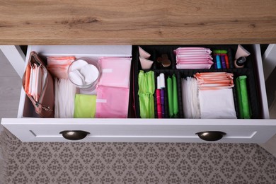 Open cabinet drawer with menstrual pads, tampons and skin care products indoors, above view