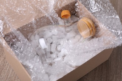 Flask with bubble wrap and packaging foam in cardboard box on wooden table, closeup