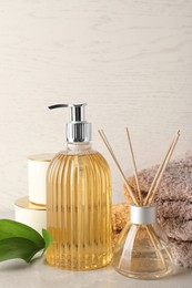Photo of Stylish soap dispenser, air freshener, towels and leaves on light table