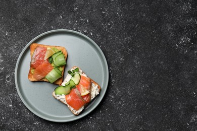 Tasty toasts with salmon, cream cheese and cucumber on black table, top view. Space for text